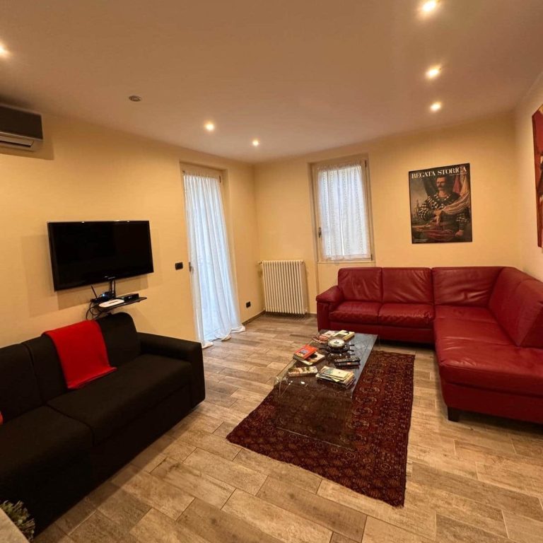 Living room with red sofa, black armchair and TV on light wall.