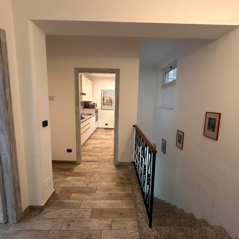 Corridor with wooden flooring, a stair railing, and a view into a kitchen.