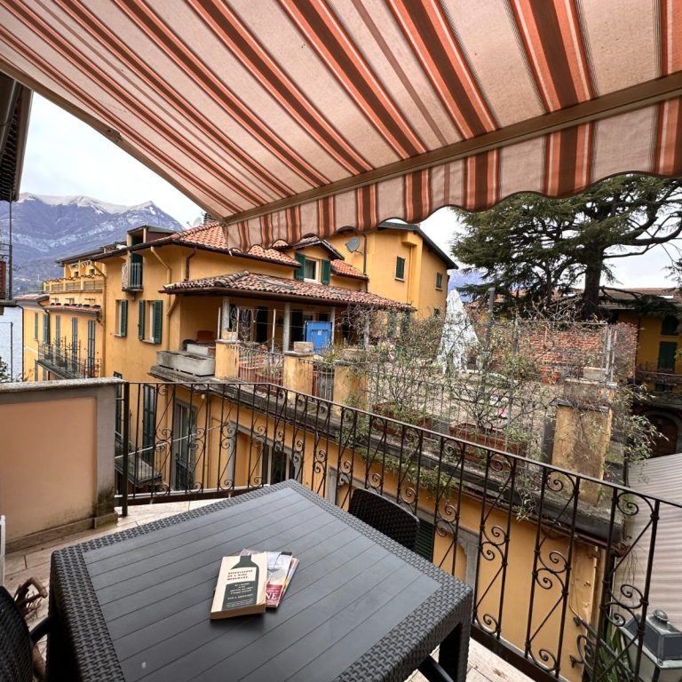 View of Bellagio houses with table, striped awning and colorful houses against the mountain backdrop.